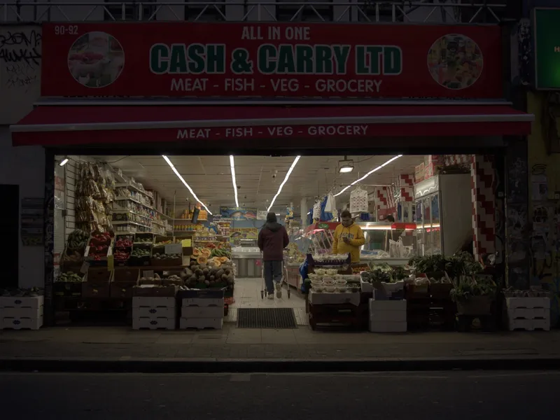 An all-in-one cash and carry lit from within at night, produce crates stacked across the pavement