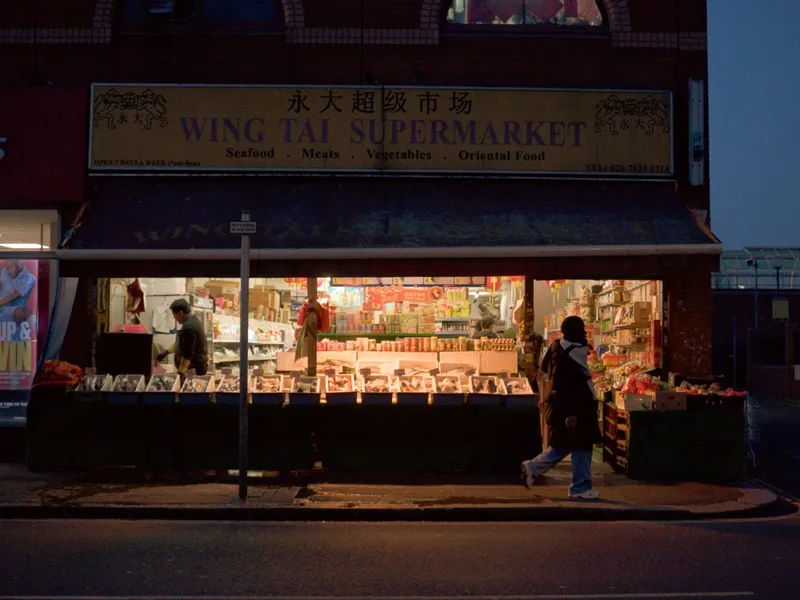 Wing Tai supermarket at blue hour, a lone figure walking past the illuminated shopfront