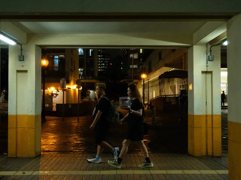 Figures running through a lit corridor at night, seen from the dark