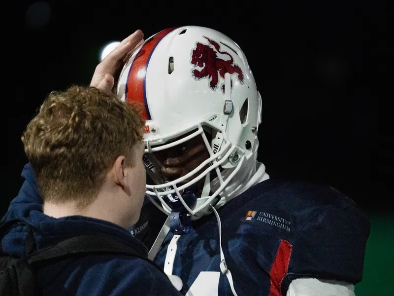 A player in a helmet turning toward the sideline, another figure close behind