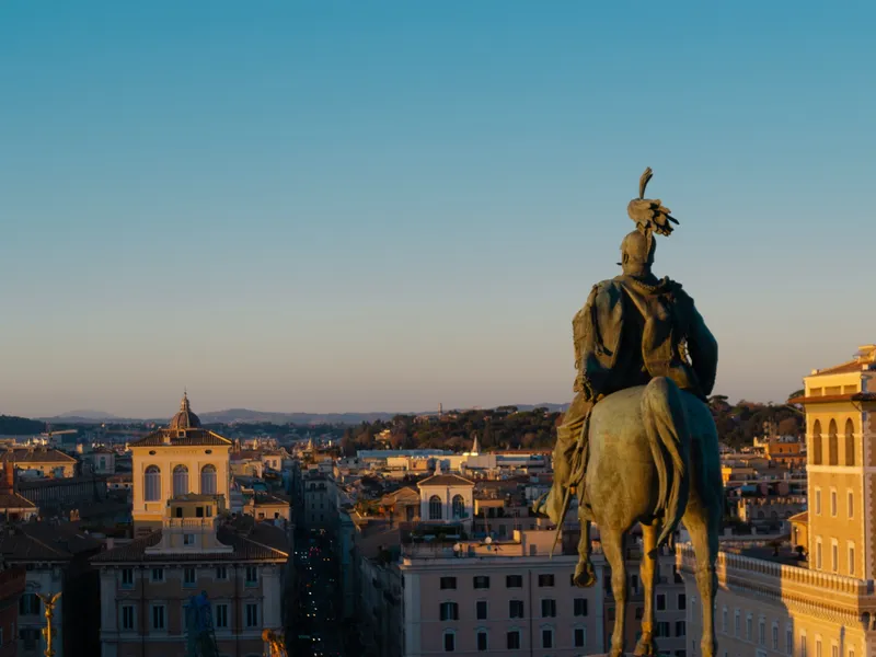A rooftop statue silhouetted against Rome at sunset