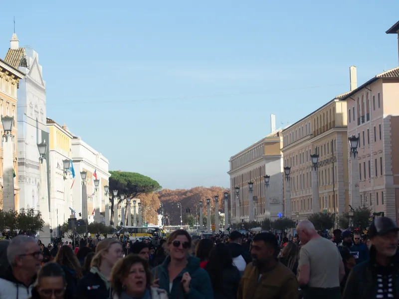 A crowded street approaching the Vatican, tourists filling the road between tall buildings